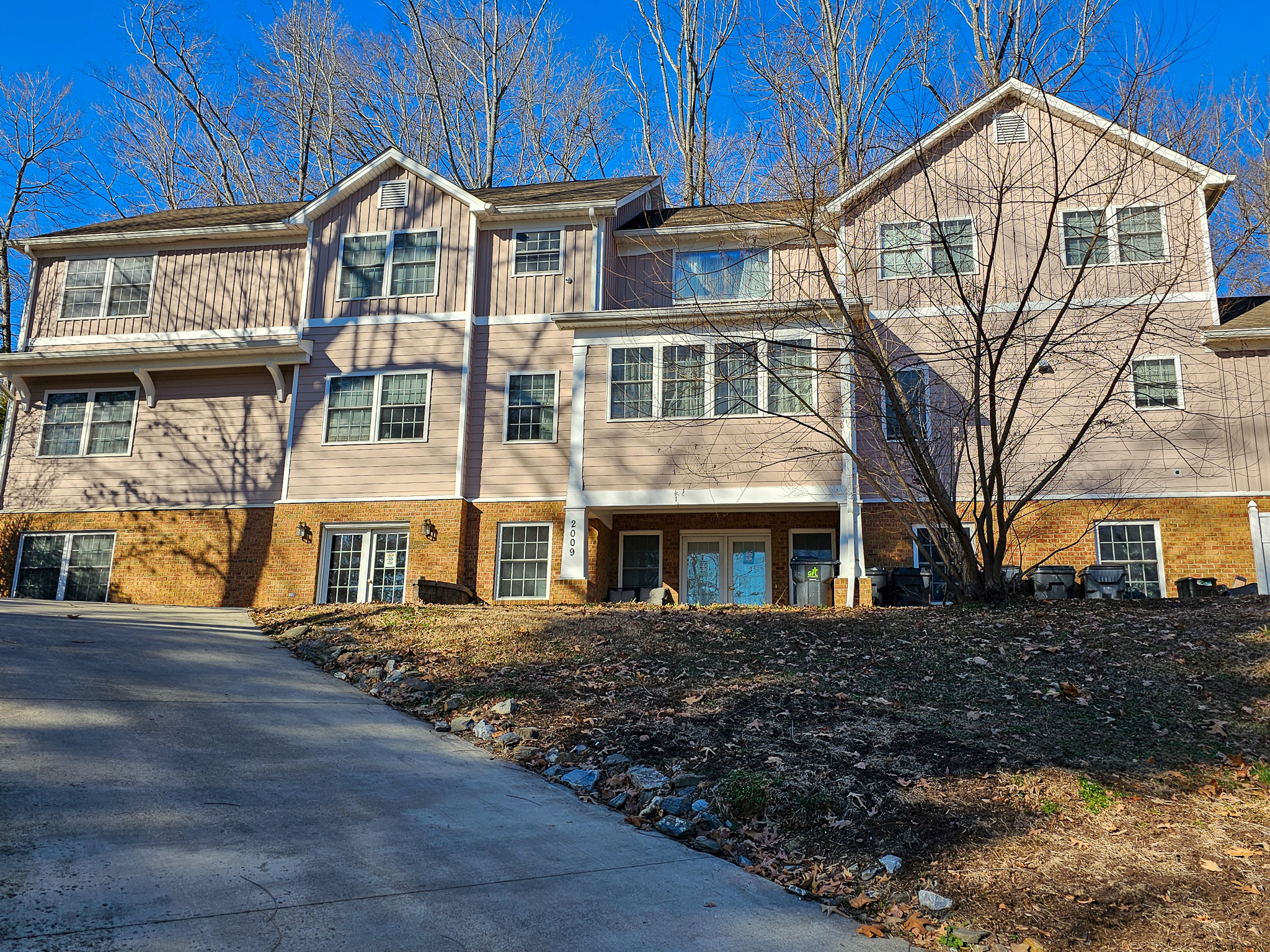 Boonsboro Group Home in Lynchburg, Virginia: a large multi‑story house with light siding and brick accents sits on a sloped yard beside a concrete driveway.