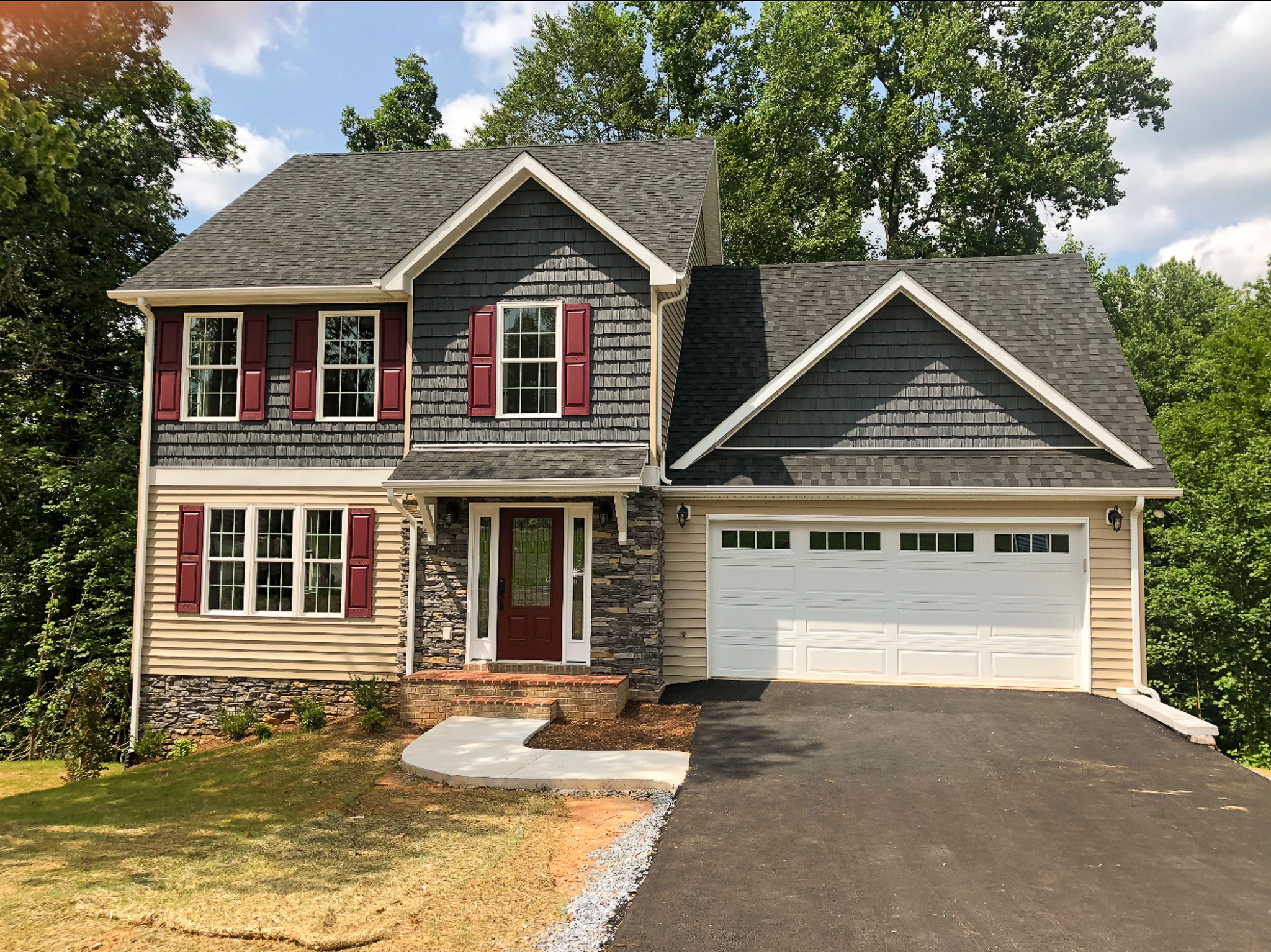 Two‑story house with gray siding, red shutters, stone accents, and a white two‑car garage, set beside a freshly paved driveway and surrounded by trees belonging to Sponsored Residential Providers Tonya and Michael Stewart in Lynchburg, Virginia.