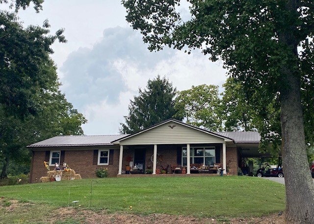 Single‑story brick house with a covered front porch, set on a grassy lawn with mature trees belonging to Group Home Providers Susan and Archie Utt in Austinville, Virginia.