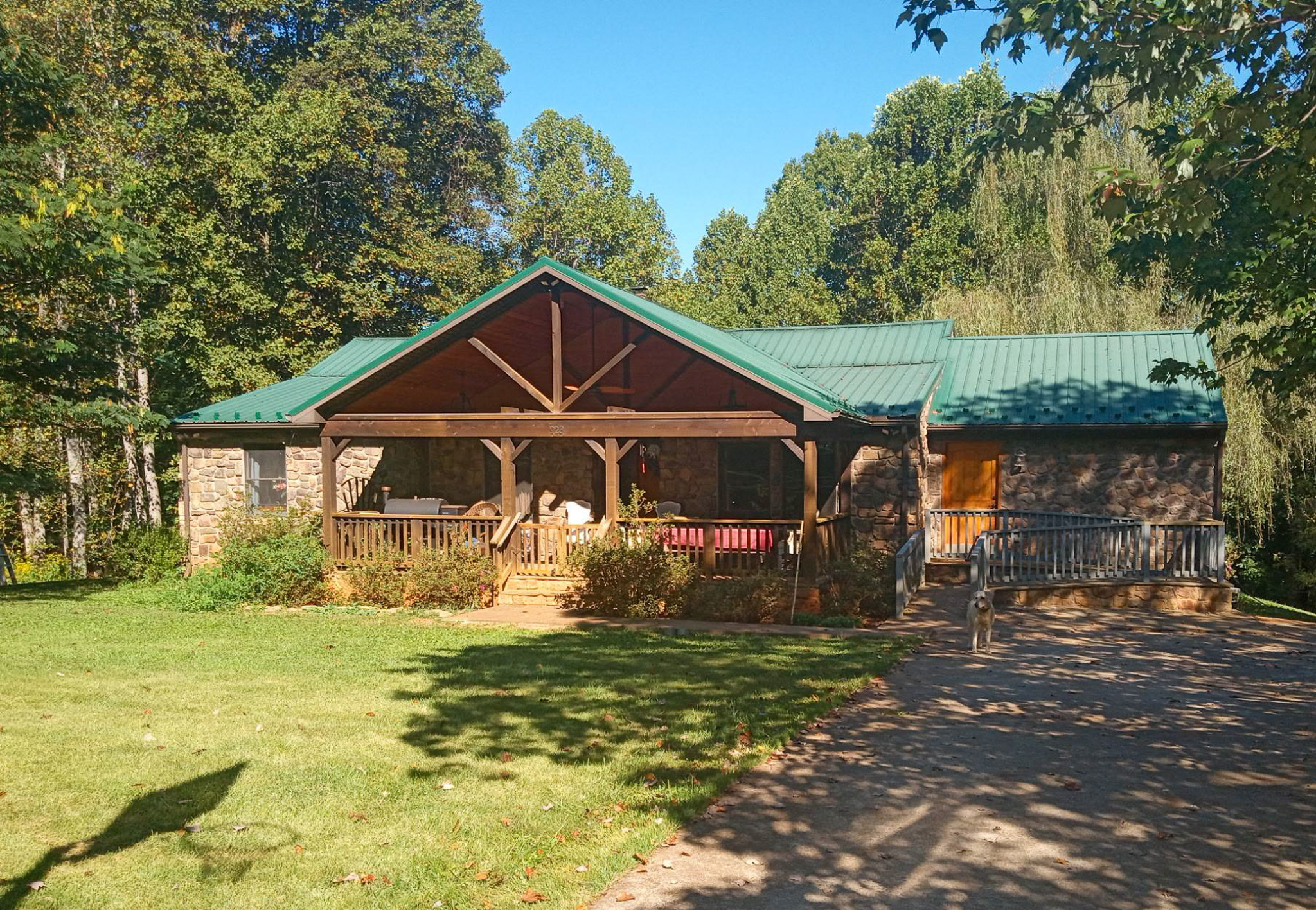 One‑story cabin‑style home with a green metal roof, large covered porch, and surrounding trees belonging to Group Home Providers Pam and Mark Turner in Monroe, Virginia.