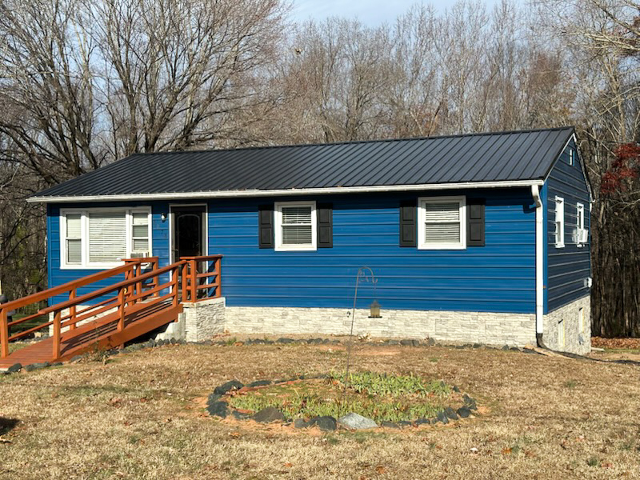 Small blue house with a black metal roof, white trim, and a wooden ramp leading to the front door, set against leafless trees belonging to Sponsored Residential Provider Phyllis Thompson in Madison Heights, Virginia.