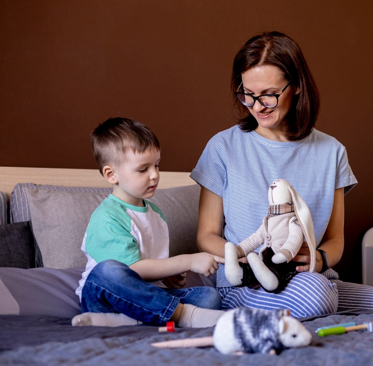 A Woman and child playing with a stuffed rabbit while sitting on a couch.