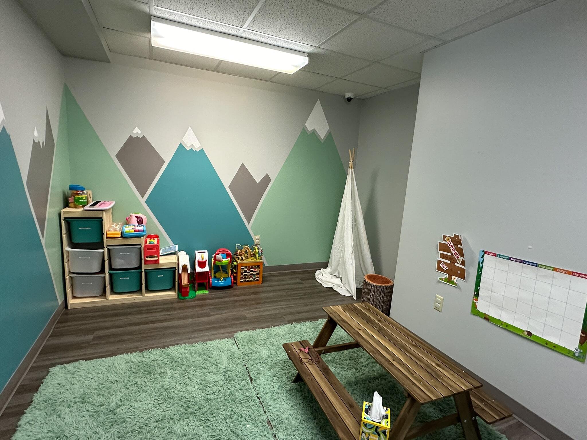 A room in the Christiansburg ABA Center featuring blue and green mountains painted on the walls, along with toys and activities