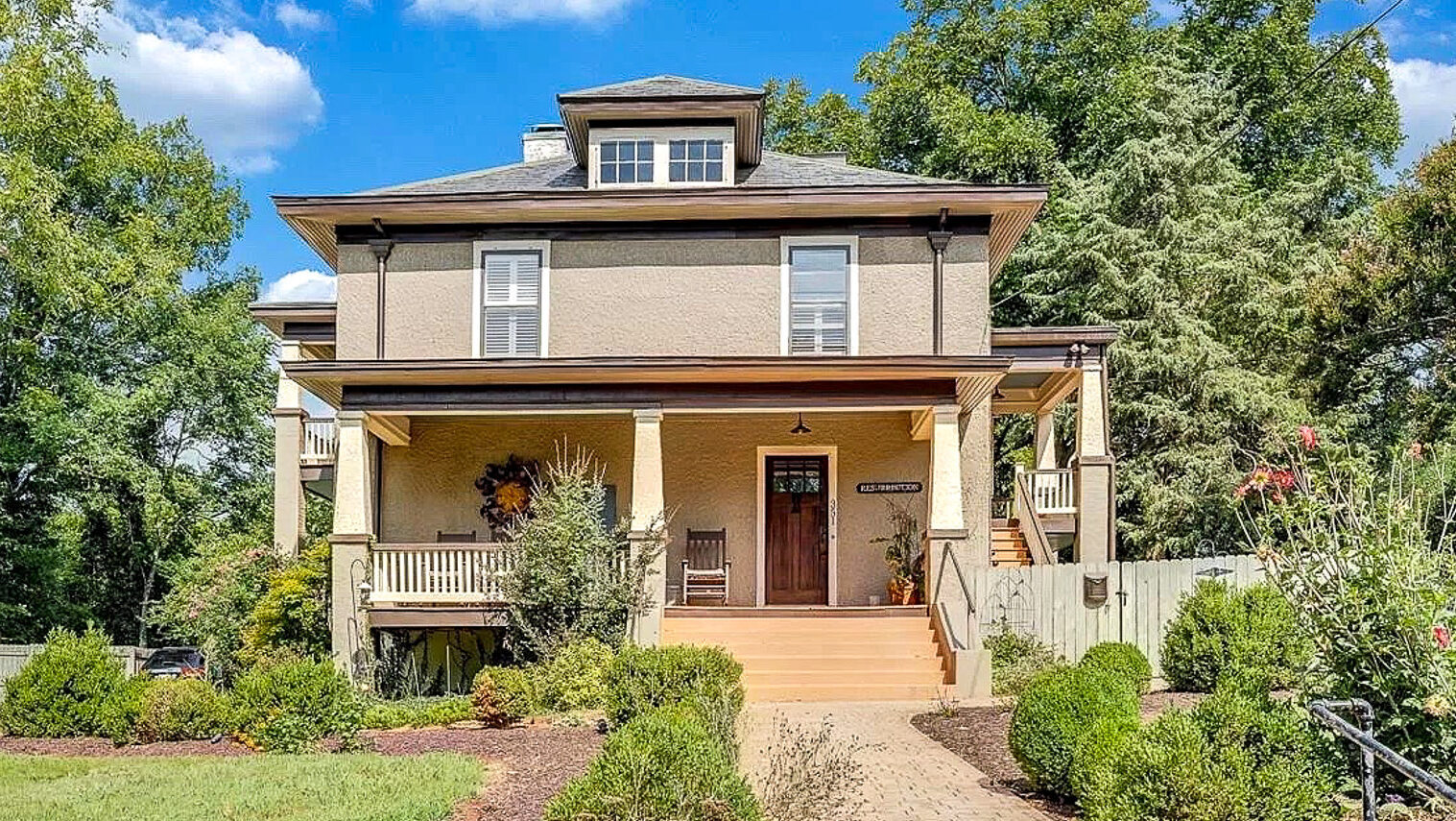 Two‑story beige house with a wide front porch, wooden steps, and landscaped shrubs along a brick walkway belonging to Sponsored Residential Providers Jeff and Sarah McLane in Lynchburg, Virginia.