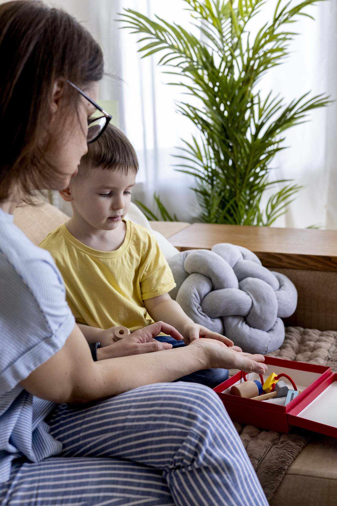 A young boy receiving home ABA therapy from a therapist using colorful toys in a red box