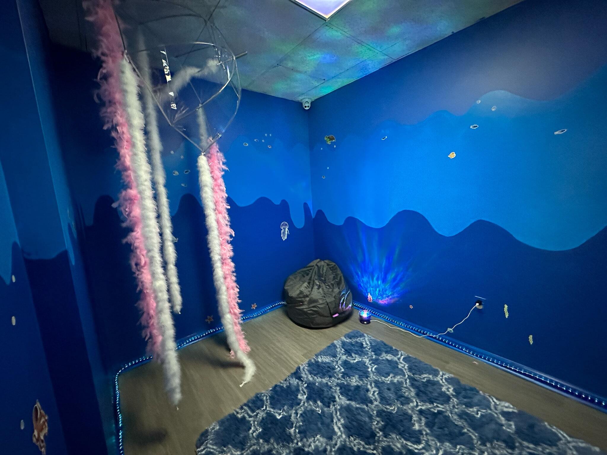 Ocean-themed room painted in shades of blue with a bean bag chair, lights, and feather boas