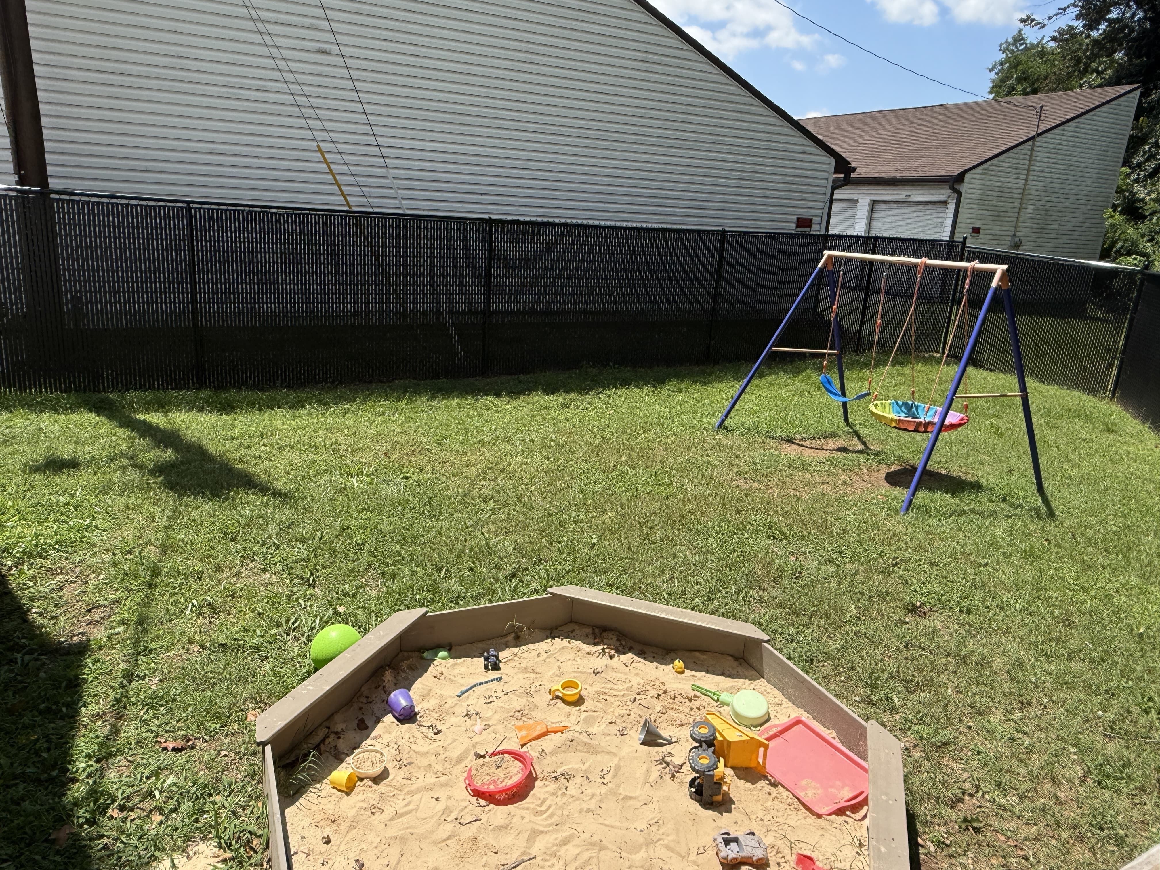 Outdoor area of the ABA Center with a swingset and sandbox filled with toys on a sunny day
